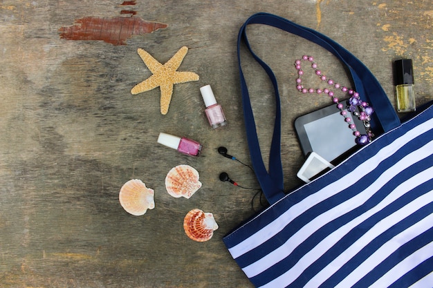 Beach bag, cosmetics and women's accessories on old wood