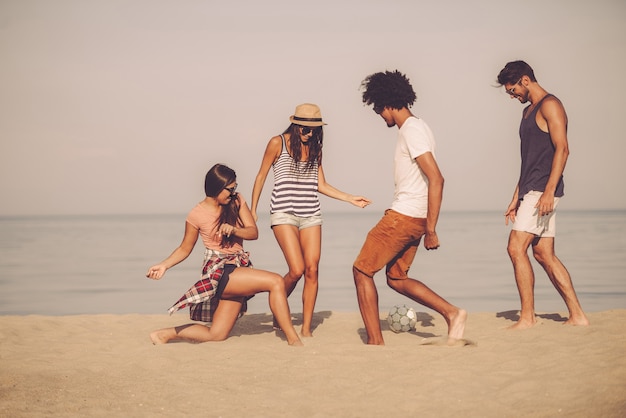 Beach ball with friends. Group of cheerful young people playing with soccer ball on the beach with sea in the background