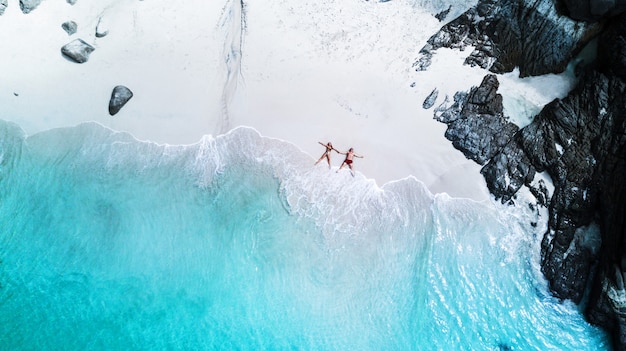 Beach drone view tropical island, white beach with waves, couple lay down on the beach