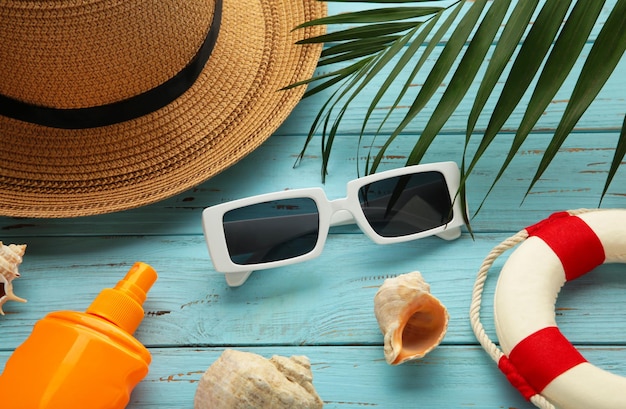 Beach flat lay accessories Sun hat palm branch sunscreen bottle and seashells on blue background Summer travel holiday concept