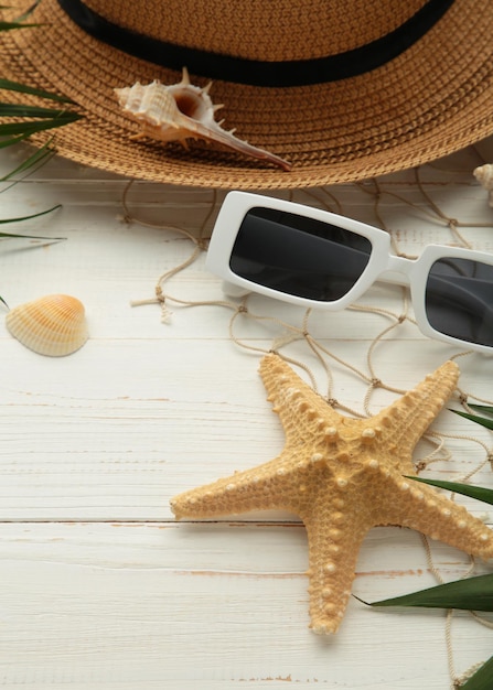 Beach flat lay accessories Sun hat palm branch sunscreen bottle and seashells on white background Summer travel holiday concept Vertical photo