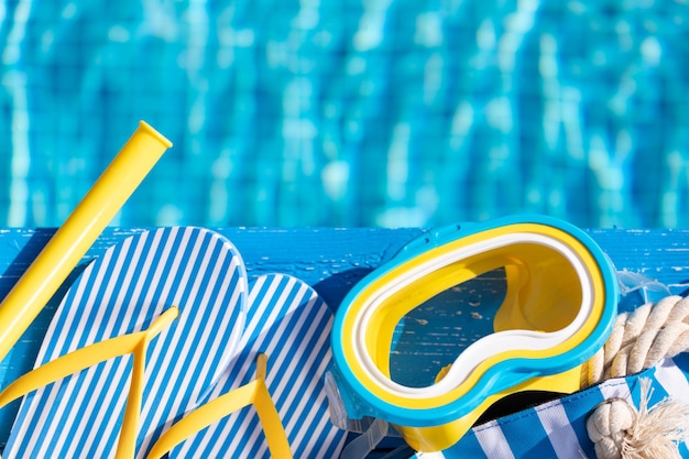 Beach flipflops and snorkel mask on blue wood against swimming pool background Summer vacation and travel concept concept