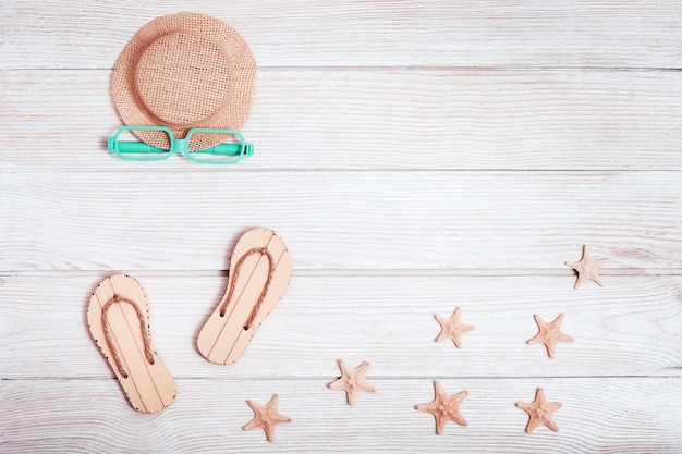 Beach lounge area with summer shoes, hat,  starfish, sunglasses on white wood surface