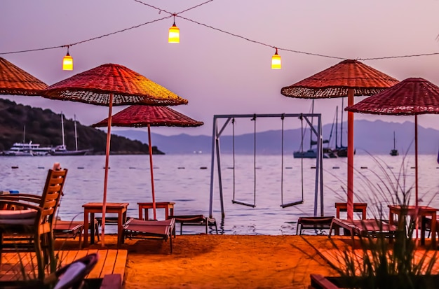 Beach umbrellas sun loungers and swings under red lanterns at sunset Summer vacation concept