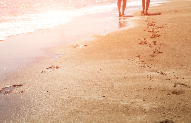 Beach, wave and women footprints at sunset time with sun flare