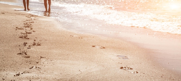 Beach wave and women footprints at sunset time with sun flare