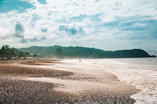 Beach with chairs and umbrellas with the jungle and mountains. Jaco, Costa Rica