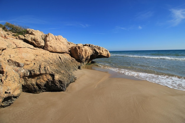 A beach with a rock formation in the foreground and a blue sky in the background Savinosa Beach