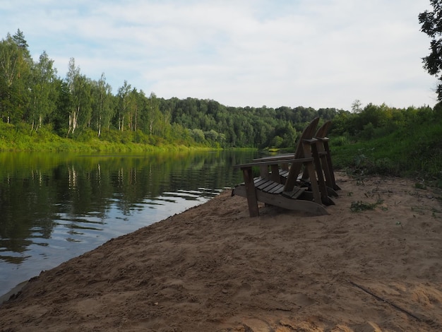 A beach with two chairs on it and a lake in the background.