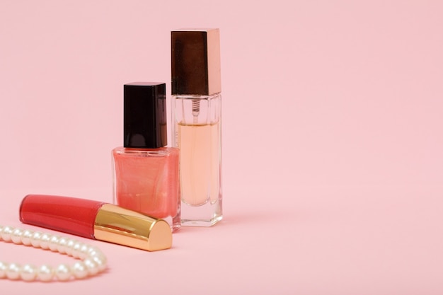 Beads, lipstick, nail polish and perfume on a pink background. Women jewelry, cosmetics and accessories.