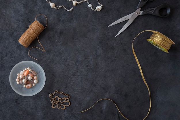 Beads necklace; brown thread; scissor; golden ribbon; beads and metal bracelet on black textured backdrop