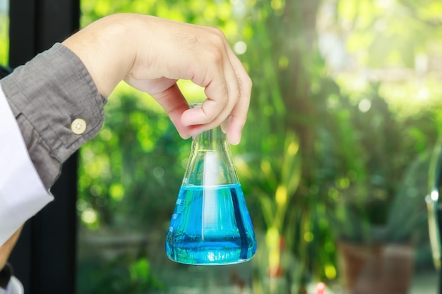 Beaker with blue experiment liquid in scientist hand on laboratory background, science concept.