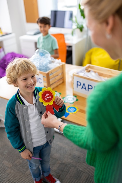 Beaming boy. Cute beaming boy feeling happy while receiving award at school after waste sorting