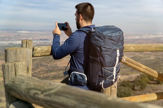 Bearded backpacker taking a photo with his smart phone from a vantage point