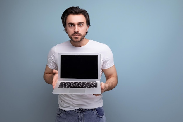 Bearded brunette man in white tshirt freelancer with laptop mockup on studio background with