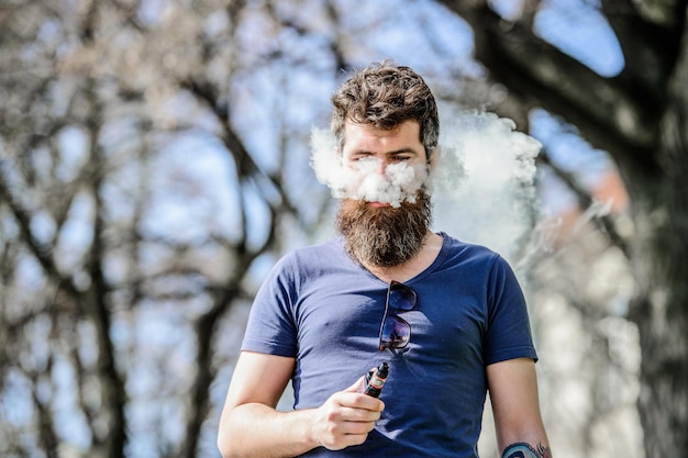 Bearded brutal male smoking electronic cigarette Mature hipster with beard man smoking ecigarette hipster man hold vaping device Health safety and addiction inhaling vapor Perfect beard