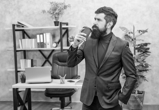 Bearded businessman drinking takeaway coffee in the office with copy space success