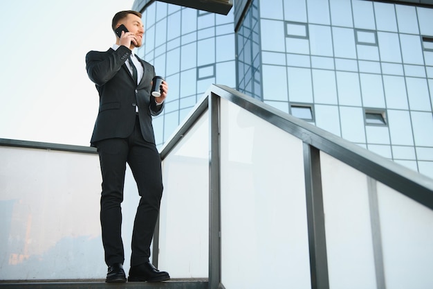 Bearded businessman in formal suit on break using mobile phone use smartphone business man standing outside on modern urban city street background with coffee cup in downtown outdoors copy space