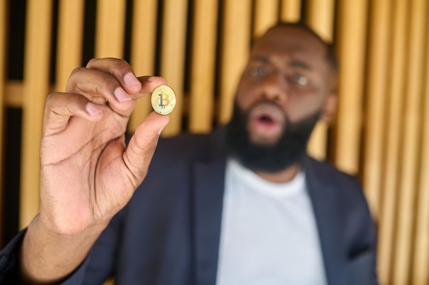 A bearded dark-skinned man holding a bitcoin