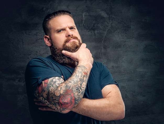 Bearded fat male with tattoo on arms posing over grey background.