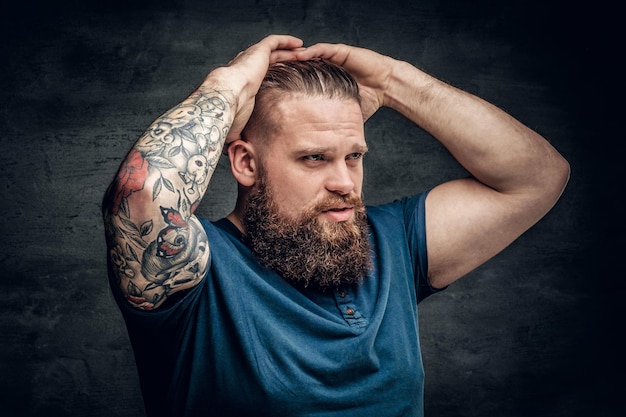 Bearded fat male with tattoo on arms posing over grey background.