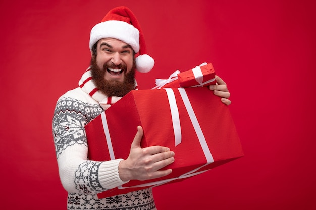 bearded guy in Christmas hat smiling and holding bunch of gift boxes