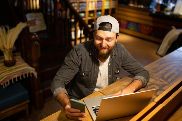 Bearded happy man uses laptop and phone in the cafe