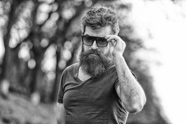 Bearded hipster brutal macho Barber concept Man bearded with mustache serious face confident nature background Bearded man with sunglasses Hipster bearded confident in dark fashionable sunglasses