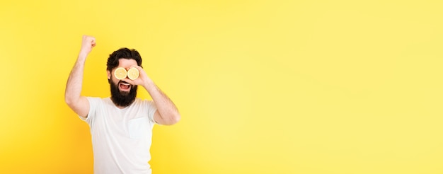 Bearded hipster man holding lemon slices in front of eyes