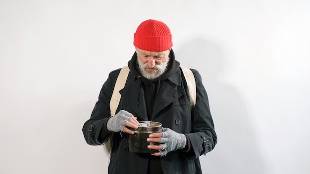 Bearded, homeless beggar old man, in a coat and hat without money on an isolated white background