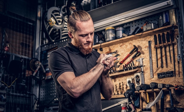 Bearded male bicycle mechanic cleans his arms after bike service manual in a workshop.