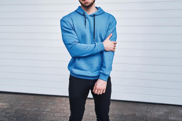 A bearded man in a blue hoodie leans against a white wall This is a mockup for logo and brand swag design easily customize it with your own graphics and text