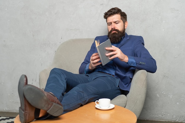 Bearded man ceo read book relaxing in armchair during rest break, reading.