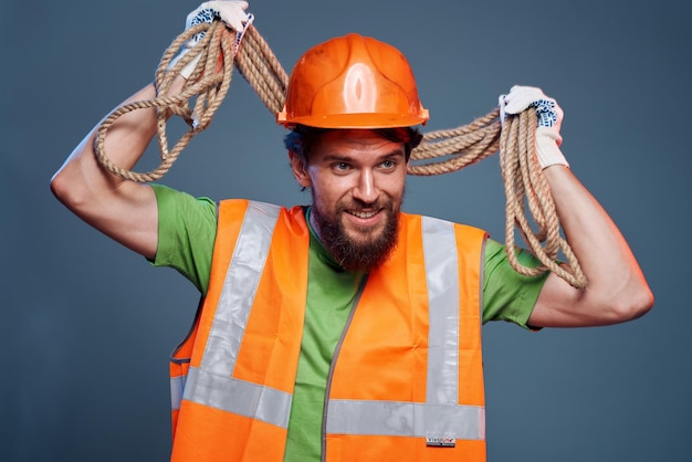 A bearded man construction worker in an orange hard hat safety rope in his hands