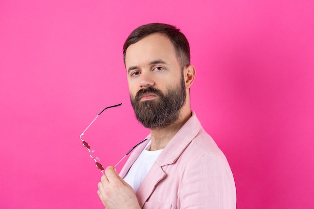 Bearded man dressed in a pink jacket with glasses Emotional studio portrait