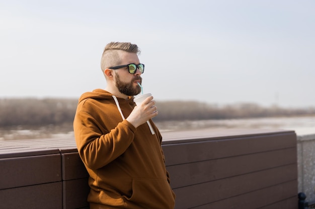 Bearded man drinking a shake in spring promenade drinks take away and gen z or millennial youth