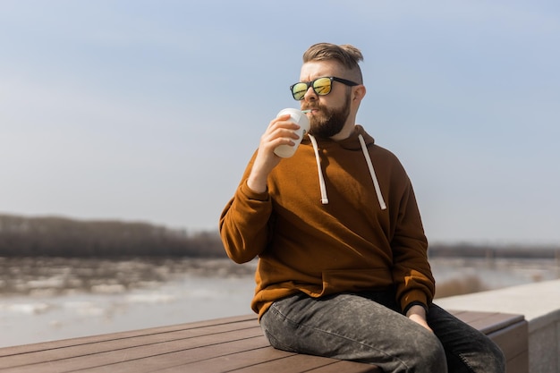 Bearded man drinking a shake in spring promenade drinks take away and gen z or millennial youth