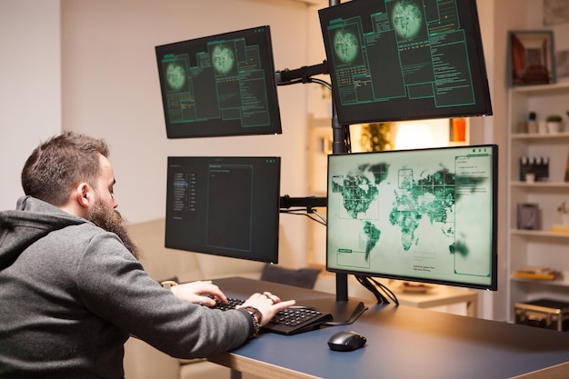 Bearded man hacking internet web sites working on computer with multiple screens.