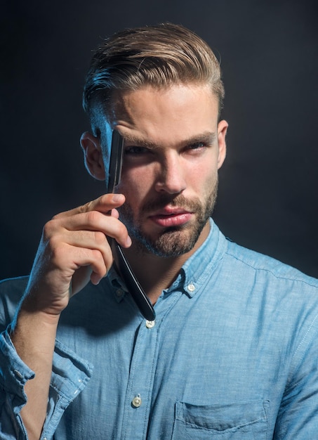 Bearded man having shave with razor blade professional barber hold straight razor near face