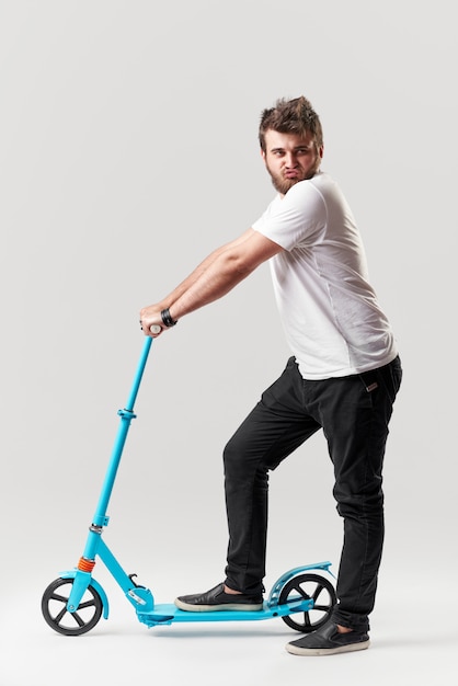 Bearded man holding the electric scooter and riding it while feeling delighted