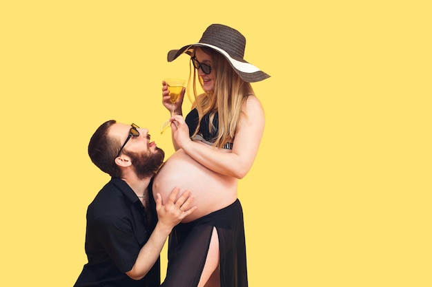 Bearded man hugging belly of pregnant wife on isolated yellow background The concept of the prenatal period A young family is expecting a baby