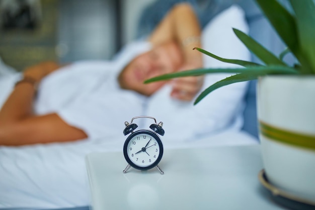 Bearded man is sleeping alone on a big and cozy bed white linens with alarm clock