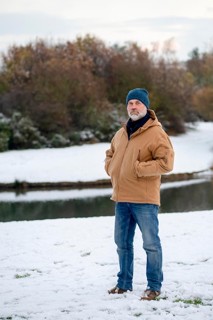 A bearded man in a jacket jeans and a hat walking in the park on a snowy winter day