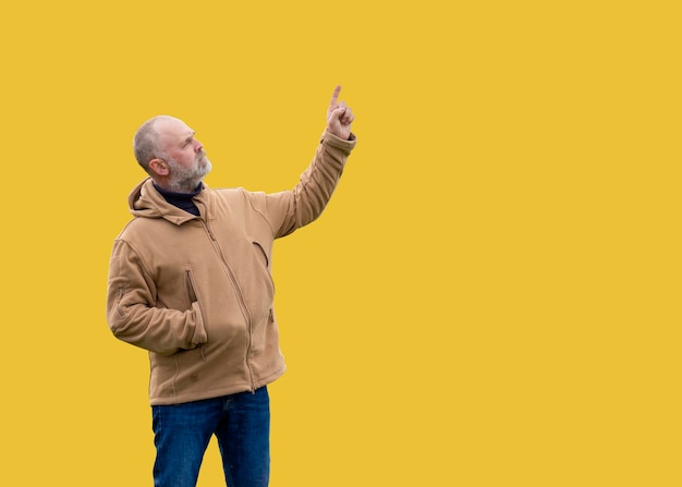 A bearded man in a jacket and jeans pointing his finger at something on a yellow background