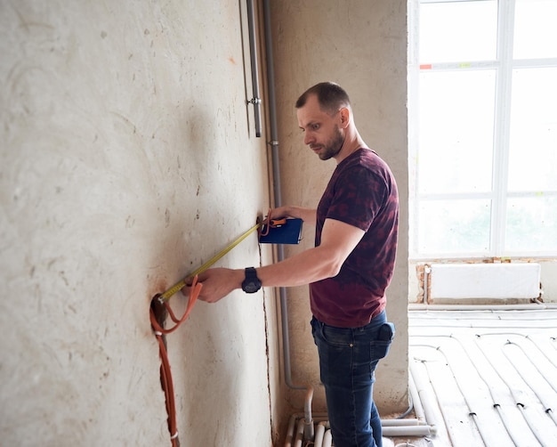 Bearded man measuring wall in empty room