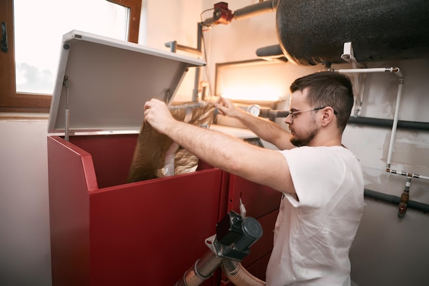 Bearded man puts wood pellet from the bag into the heating boiler oven Sustainable future concept