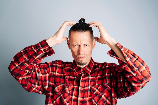 A bearded man in a red plaid shirt touches his head