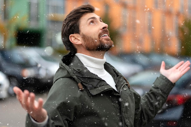 Bearded man rejoices in the snow tries to catch snowflakes The young man looks up