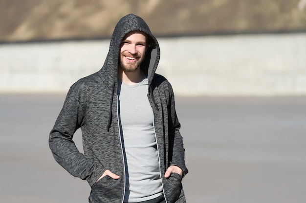 Bearded man smile in hood on sunny outdoor, fashion. Macho happy smiling in sweatshirt, casual style. Mens fashion, style, sportswear. Lifestyle for active and healthy man, sport.