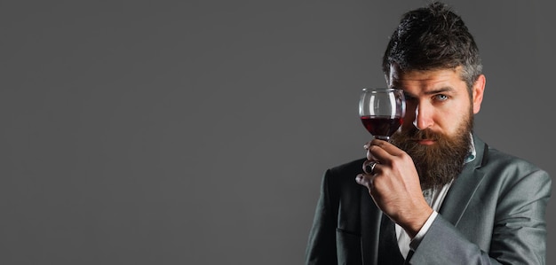 Bearded man in suit with glass of red wine tasting alcohol male sommelier with wineglass